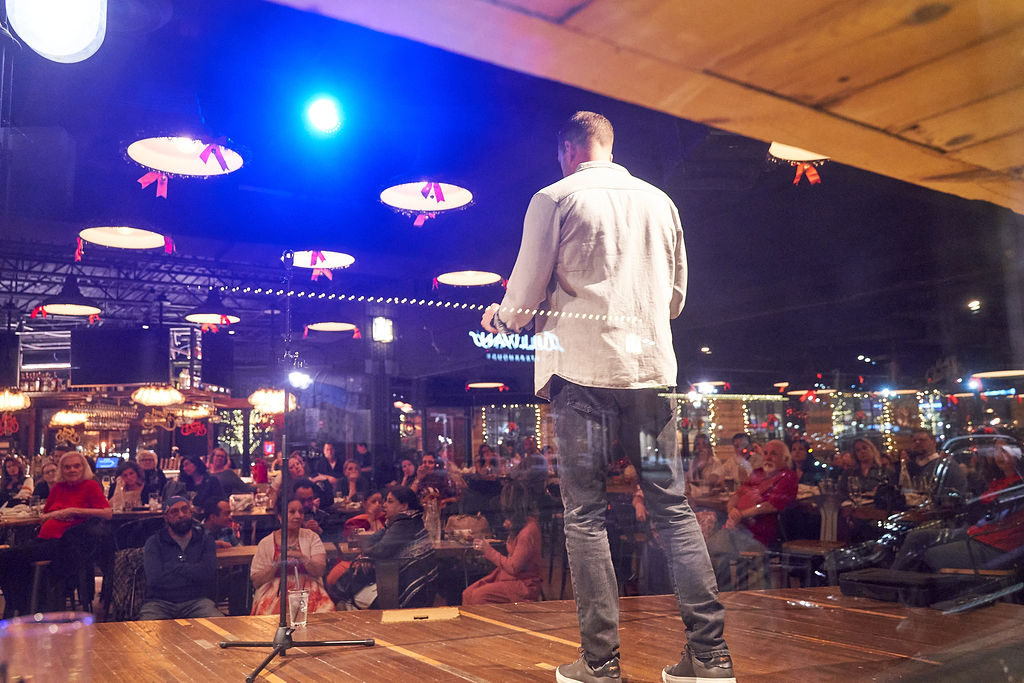 A storyteller on stage at Empire Burgers + Brew with a full audience listening